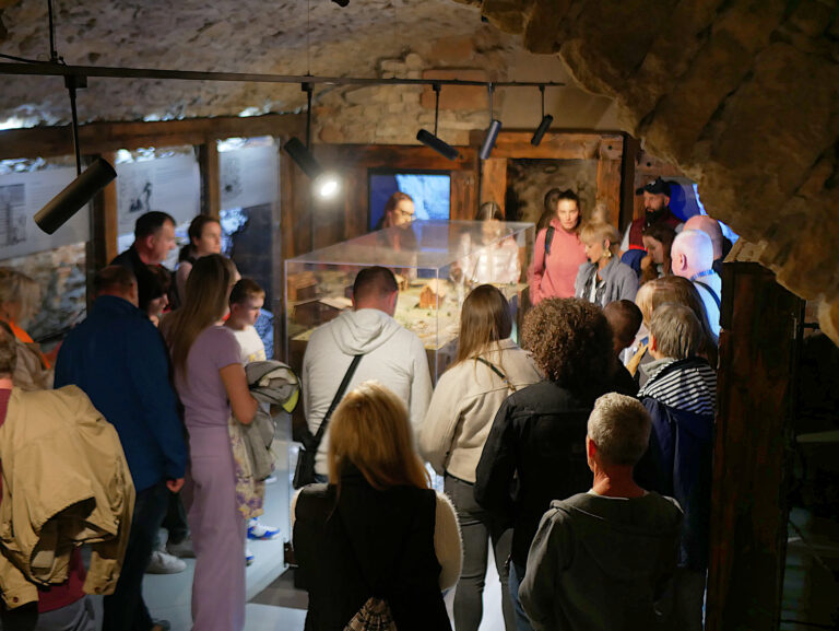 Grupa zwiedzających podczas wydarzenia noc muzeów; w tle przewodniczka opowiadająca o historii górnictwa na ekspozycji podziemi kwartału królewskiego